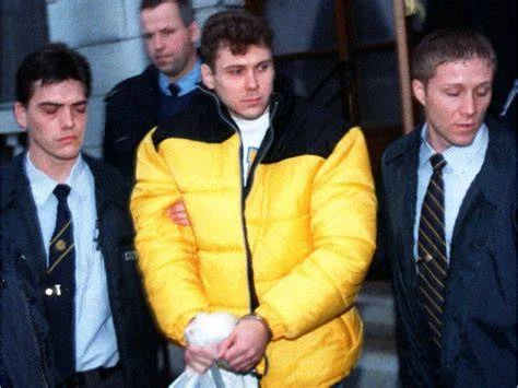Paul Bernardo, handcuffed and in a yellow jacket, escorted by plainclothes officers