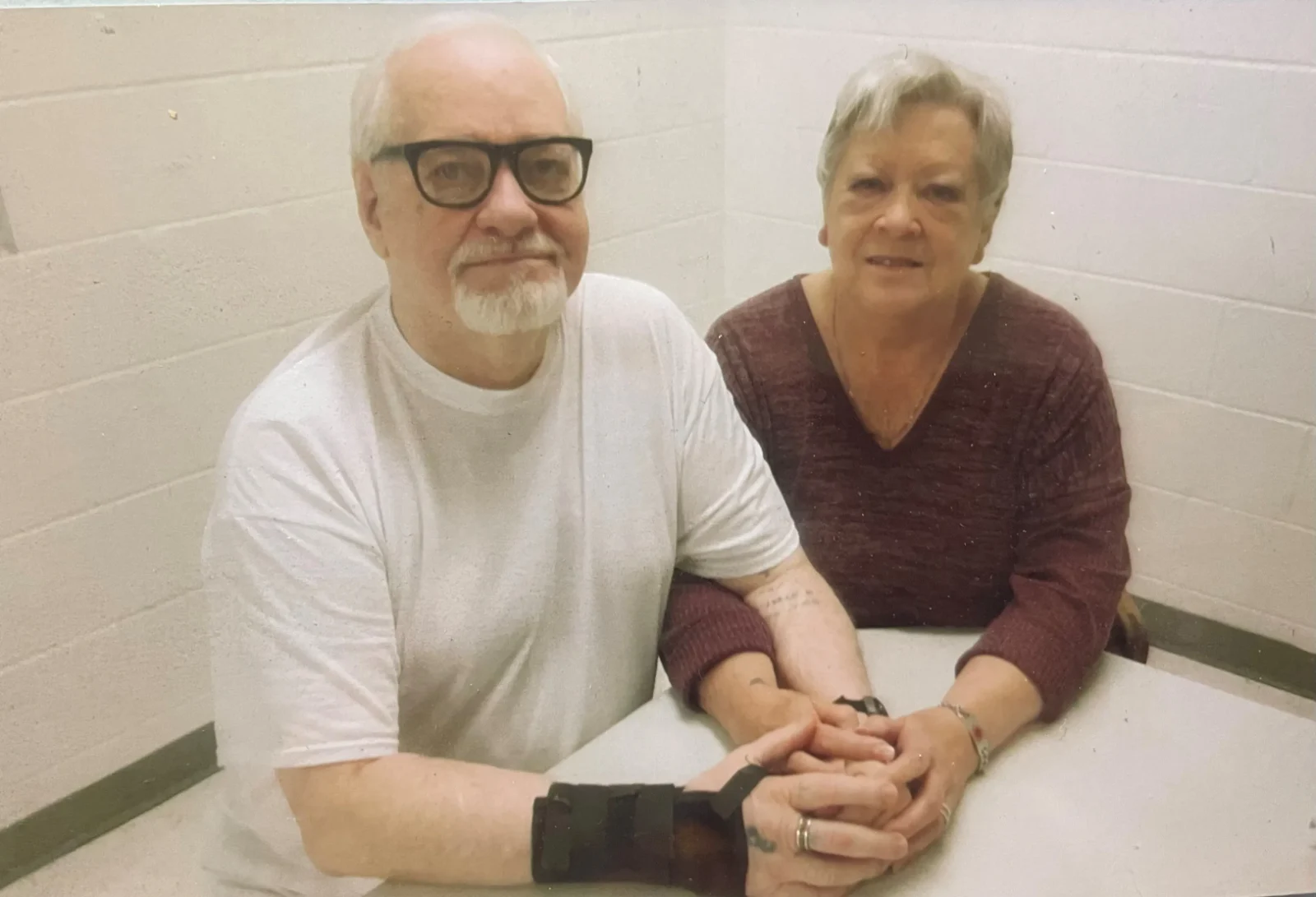 Thomas Creech, white-bearded and in glasses, seated in prison with a visitor