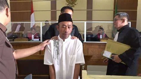 Slamet Tohari, in a white shirt and black cap, standing in an Indonesian courtroom