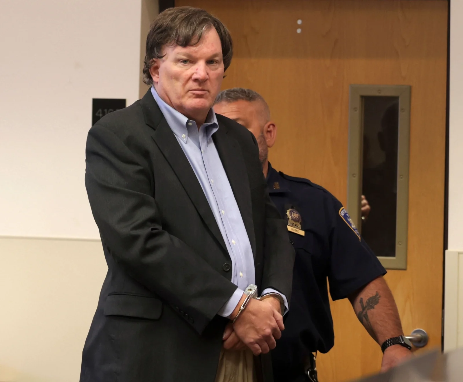 Rex Heuermann, handcuffed and in a dark suit, escorted by a court officer