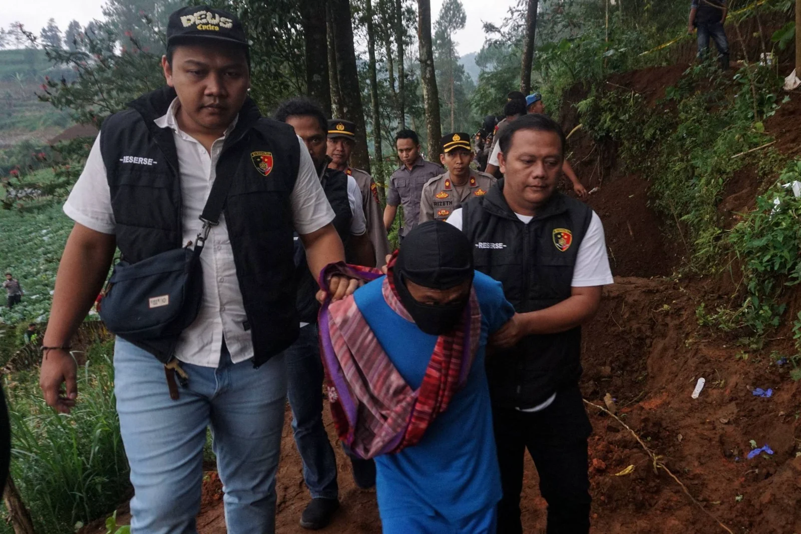 Police escort Slamet Tohari, in blue, through a wooded area