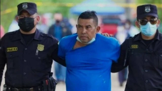 Hugo Osorio, in a blue shirt, escorted by masked Salvadoran police officers