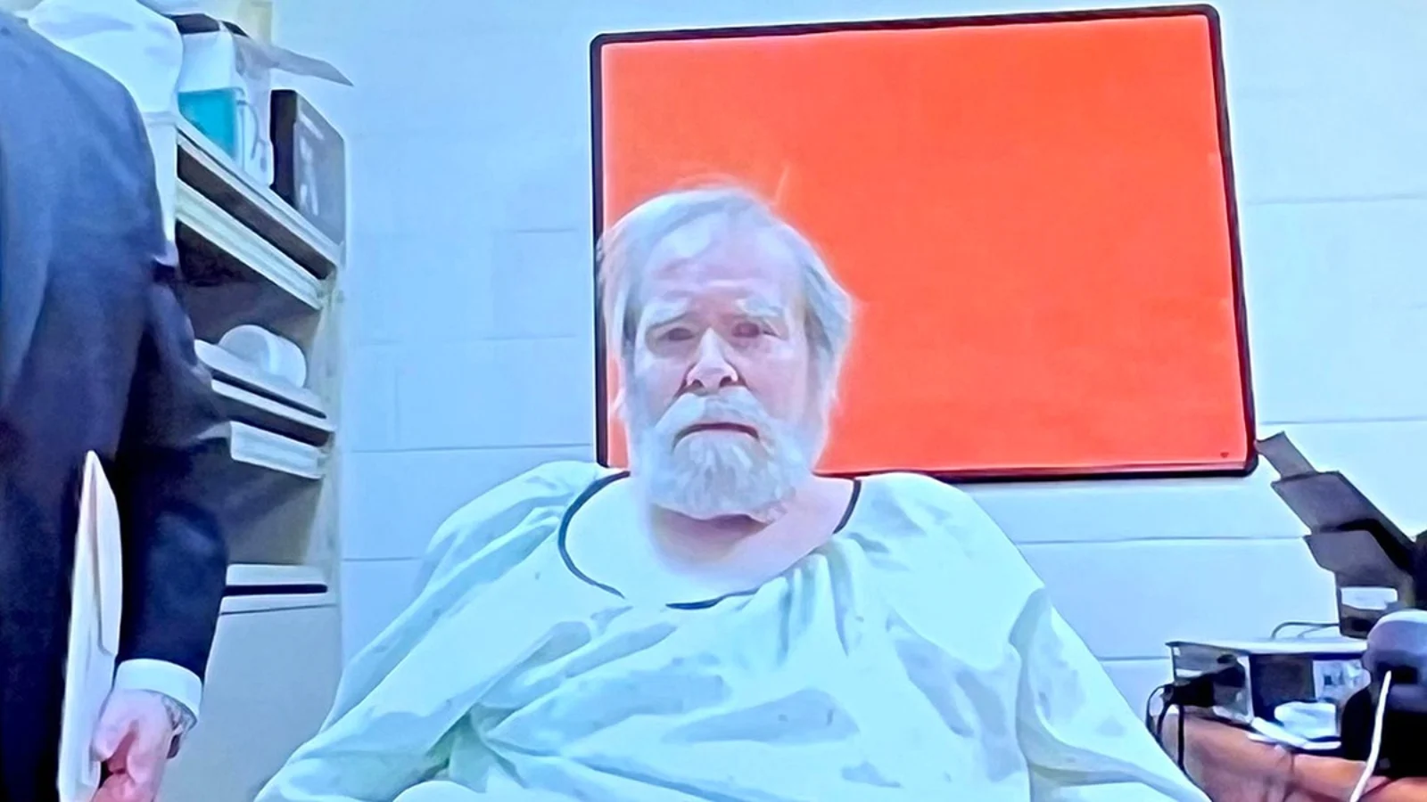 Richard Cottingham, white-haired and bearded, in light prison scrubs, seated in a prison room