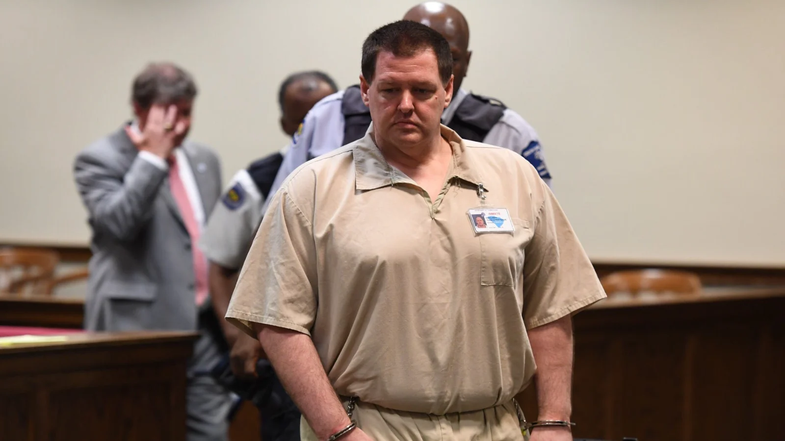 Todd Kohlhepp, handcuffed and in tan jail clothing, led through a courtroom by an officer