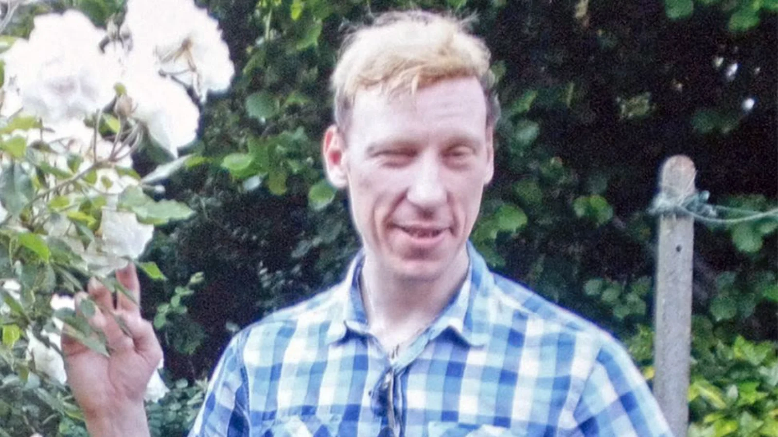 Stephen Port in a blue checked shirt standing in a garden beside white roses