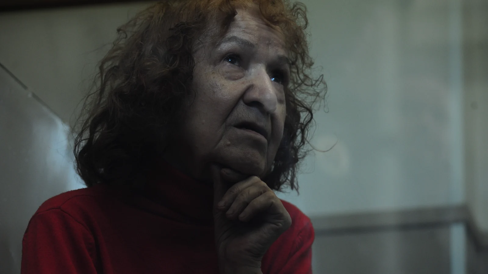 Tamara Samsonova, red-haired and in a red sweater, resting her chin on her hand inside the glass dock of a St. Petersburg court in 2015