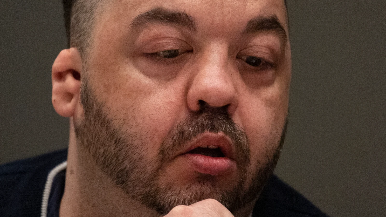 Niels Högel, bearded, resting his chin on his hand and looking down in court