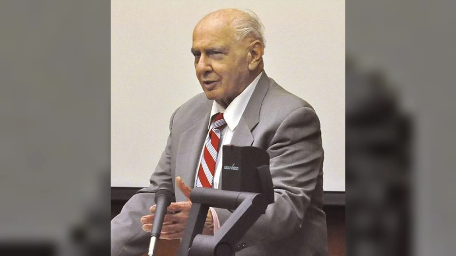 Joseph Naso, in a gray suit and striped tie, speaking at a courtroom lectern