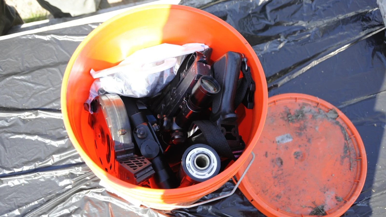 An orange bucket of gear buried by Israel Keyes in New York, opened beside its lid on a plastic sheet