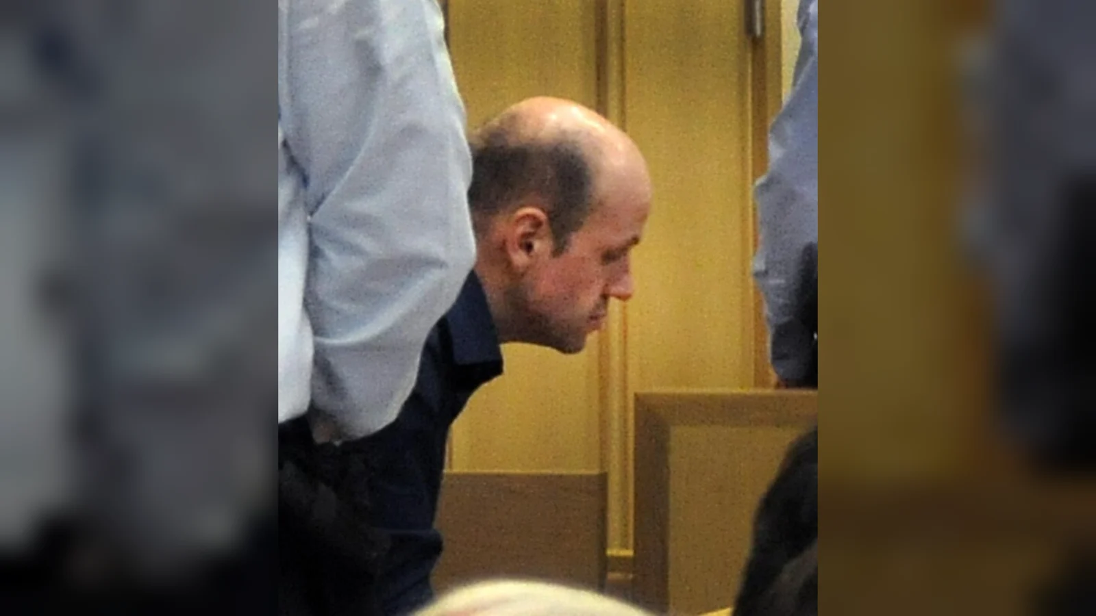 Ronald Janssen, head lowered, beside a police officer in a courtroom