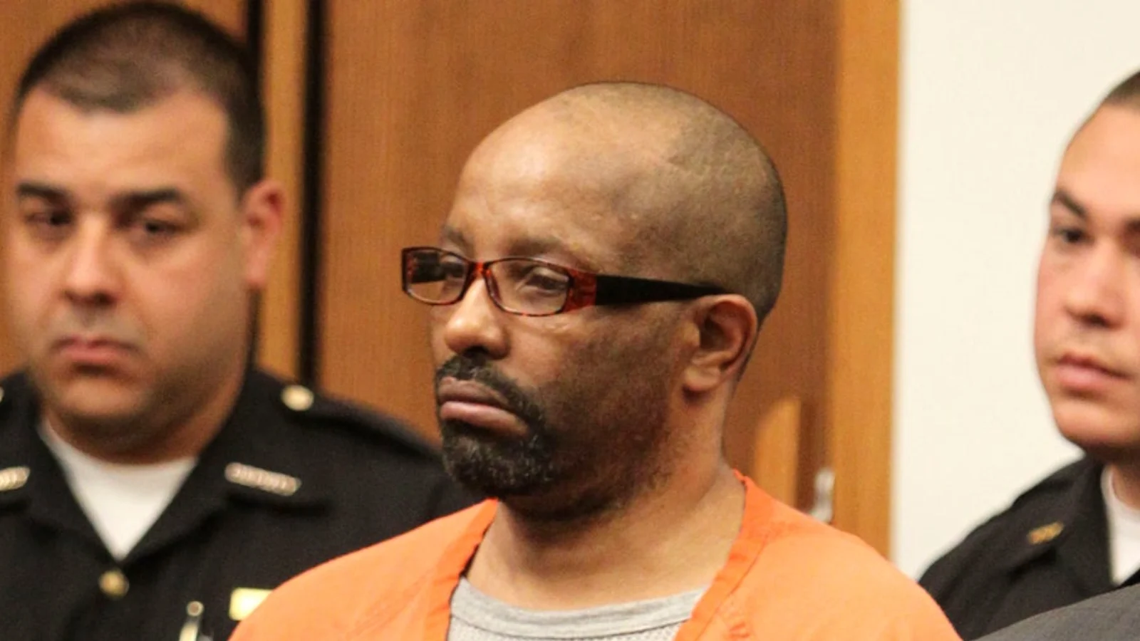 Anthony Sowell in an orange jail jumpsuit and glasses, standing between officers in a Cleveland courtroom