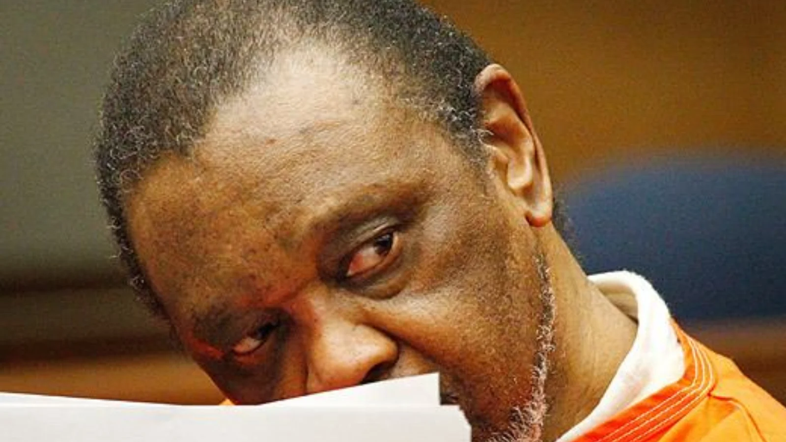 John Floyd Thomas Jr. in an orange jail jumpsuit, holding papers to his face in court