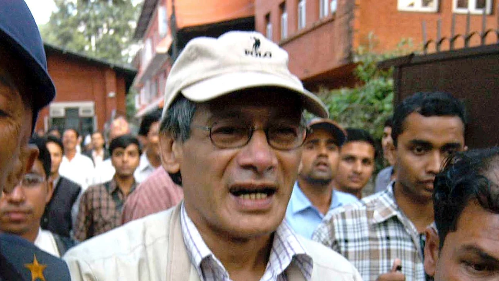 Charles Sobhraj in a cap and glasses surrounded by people outside a court in Kathmandu