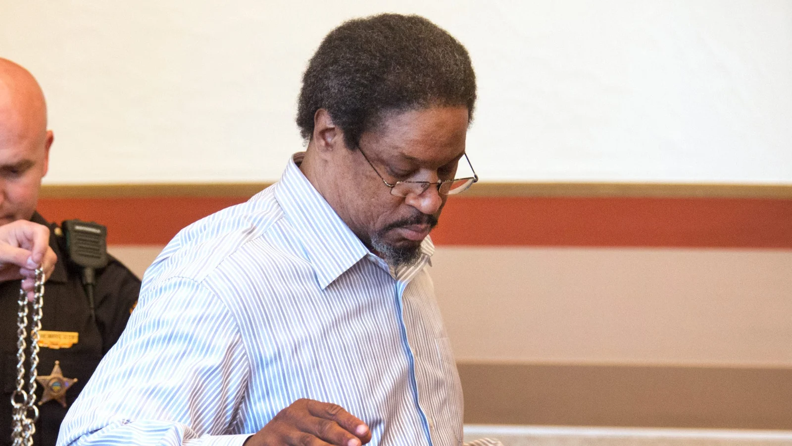 Anthony Kirkland in glasses and a striped shirt in a Hamilton County courtroom as a deputy holds his restraints