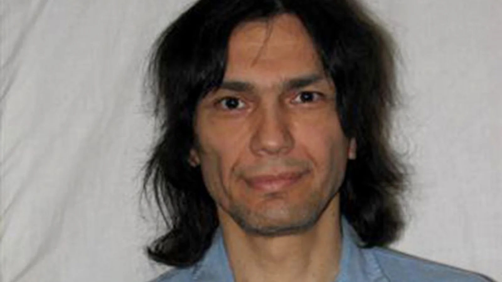 Richard Ramirez with long dark hair in a blue prison shirt, in a San Quentin photograph