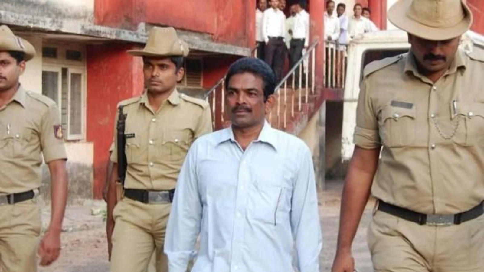 Mohan Kumar in a light blue shirt escorted by Karnataka police officers