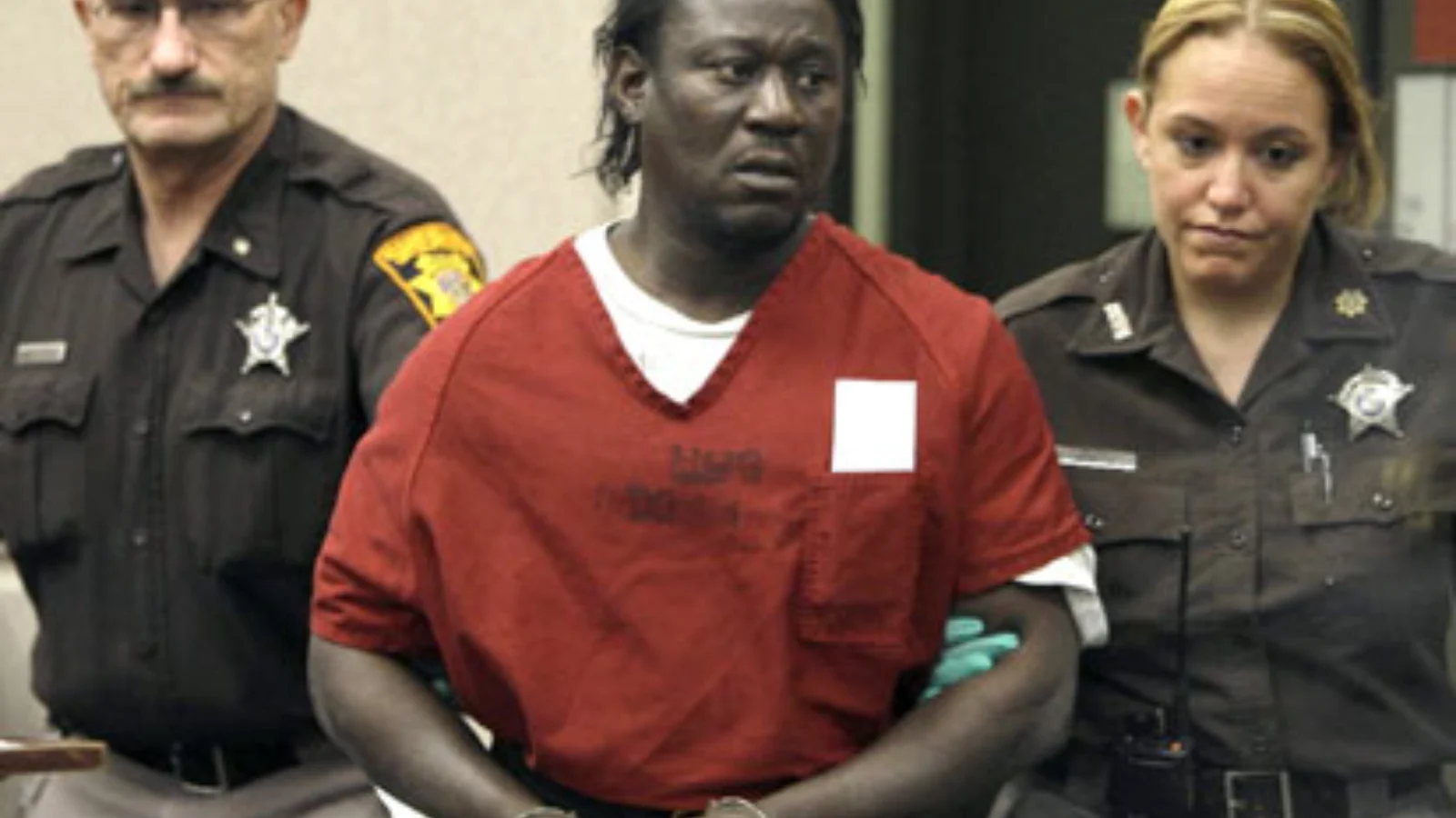Walter Ellis in a red jail jumpsuit, handcuffed between two Milwaukee County deputies in court