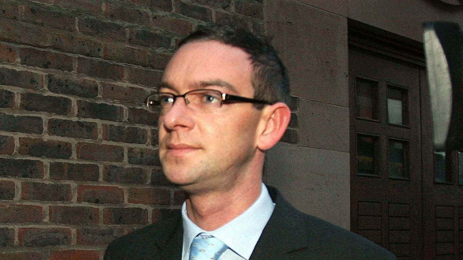 Colin Norris in glasses, a dark suit and a light blue tie outside a court building