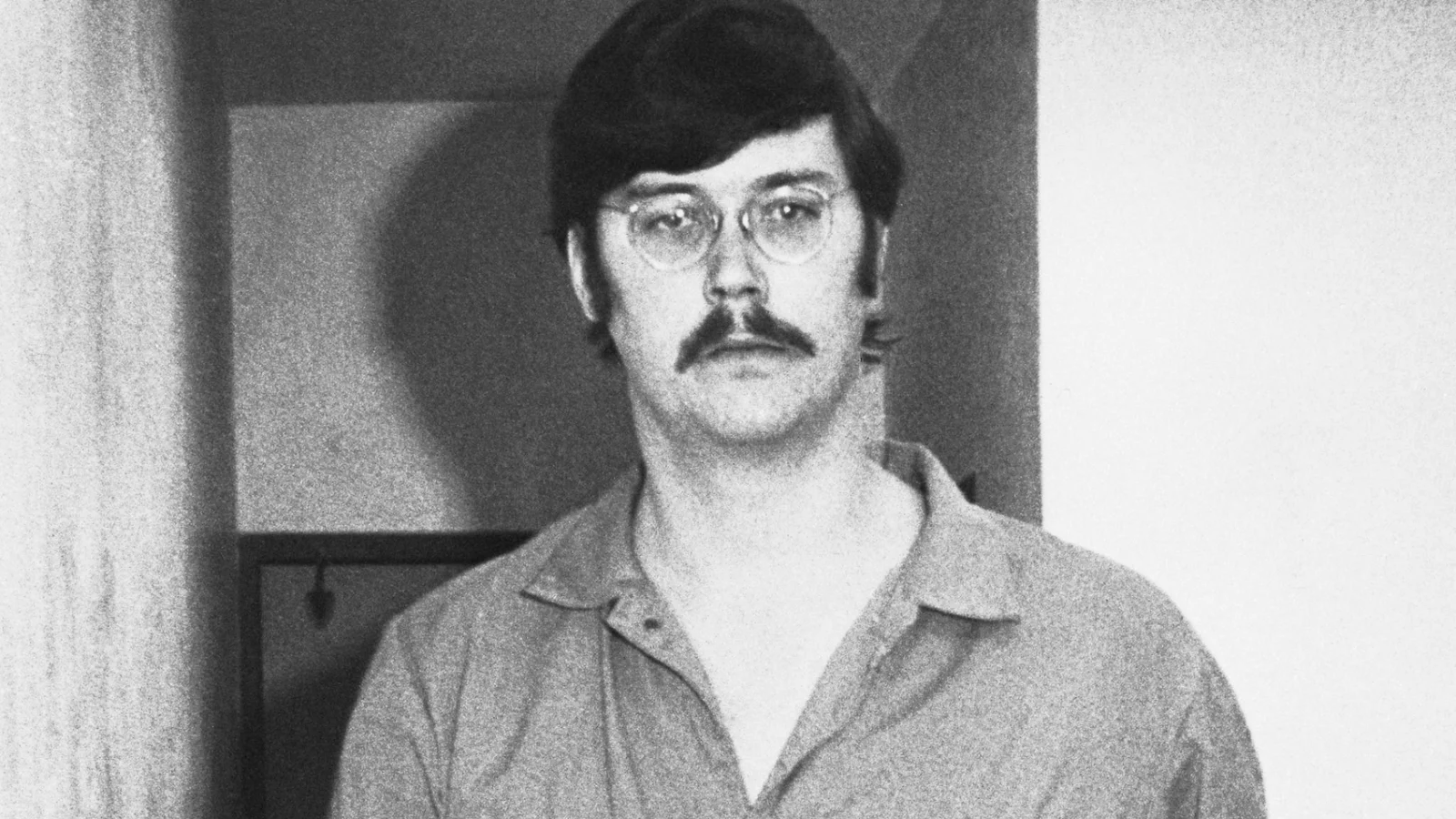 Edmund Kemper in glasses and a jail jumpsuit standing in a doorway in the 1970s