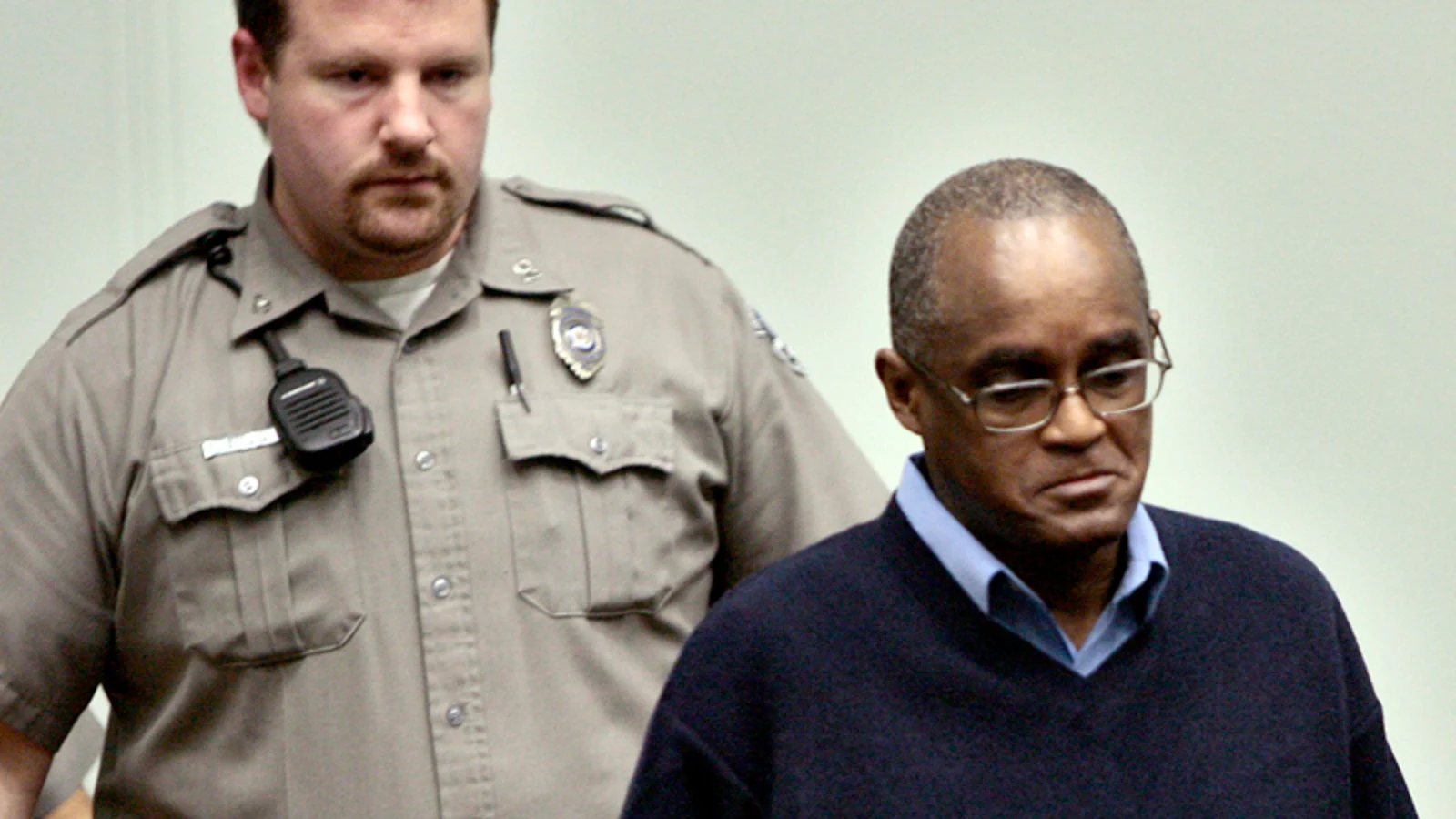 Lorenzo Gilyard in glasses and a navy sweater, led into a Kansas City courtroom by a deputy