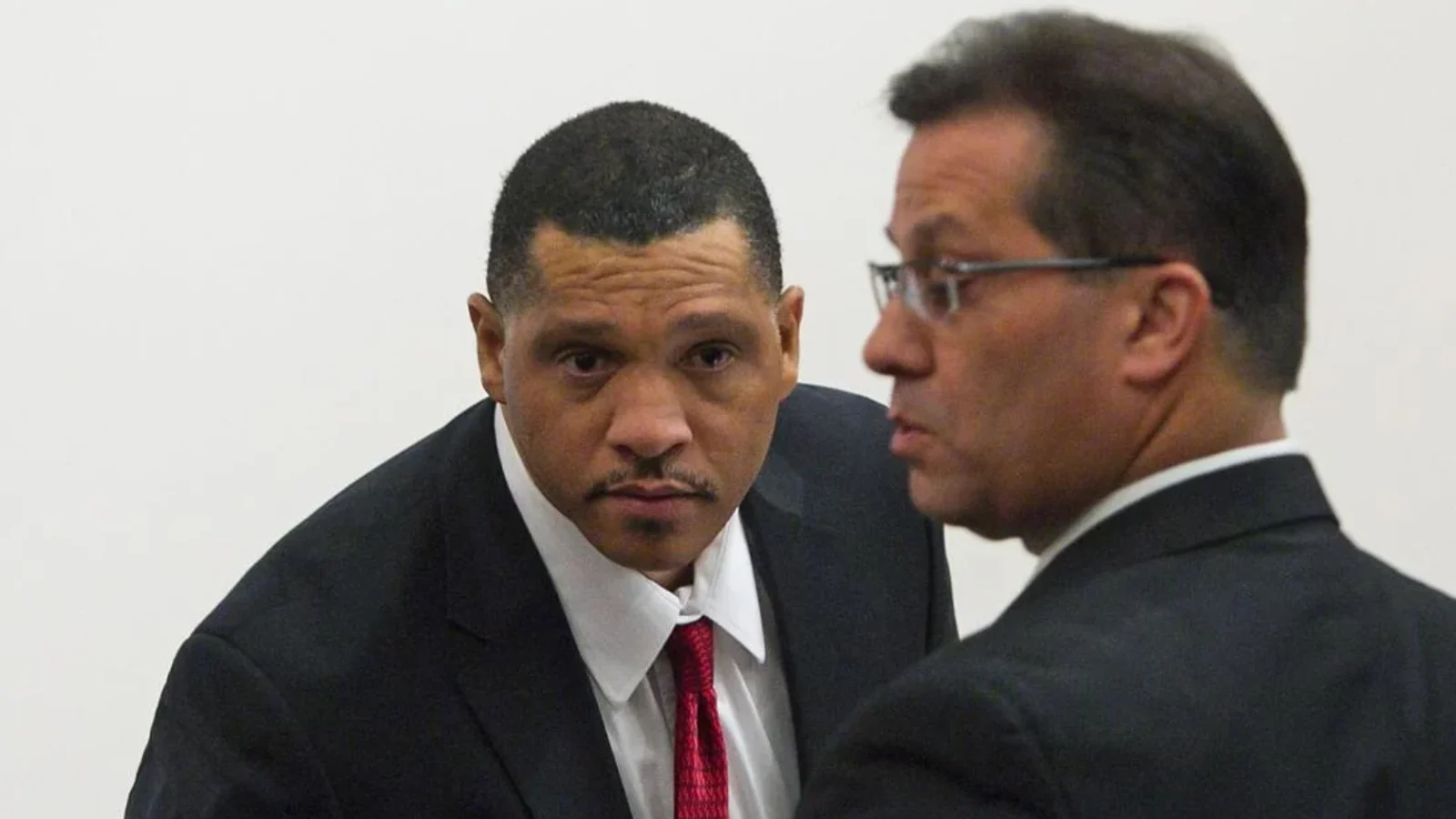 Mark Goudeau in a dark suit and red tie beside his lawyer in a Phoenix courtroom