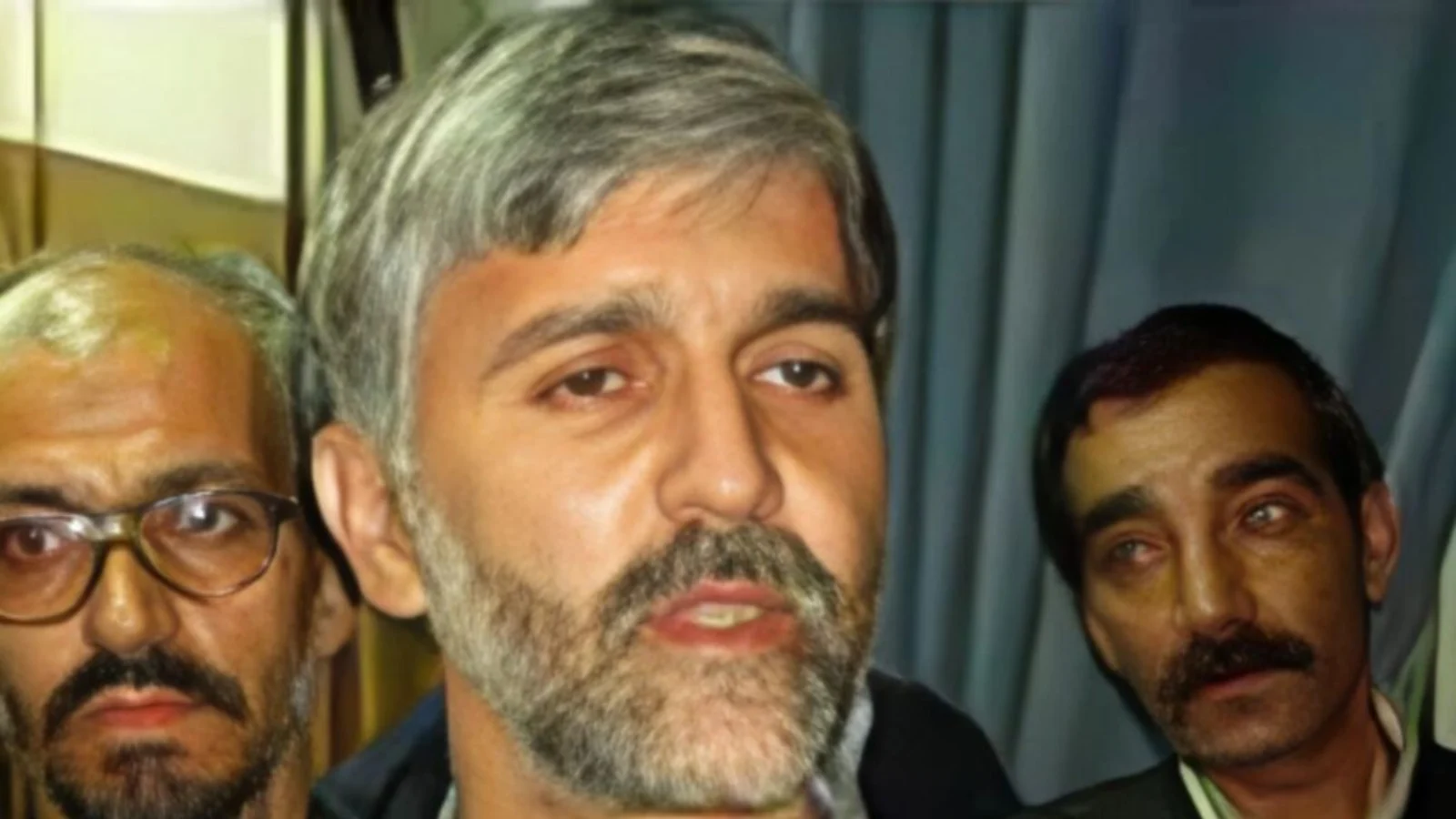 Saeed Hanaei, gray-haired and bearded, speaking to reporters with two men behind him