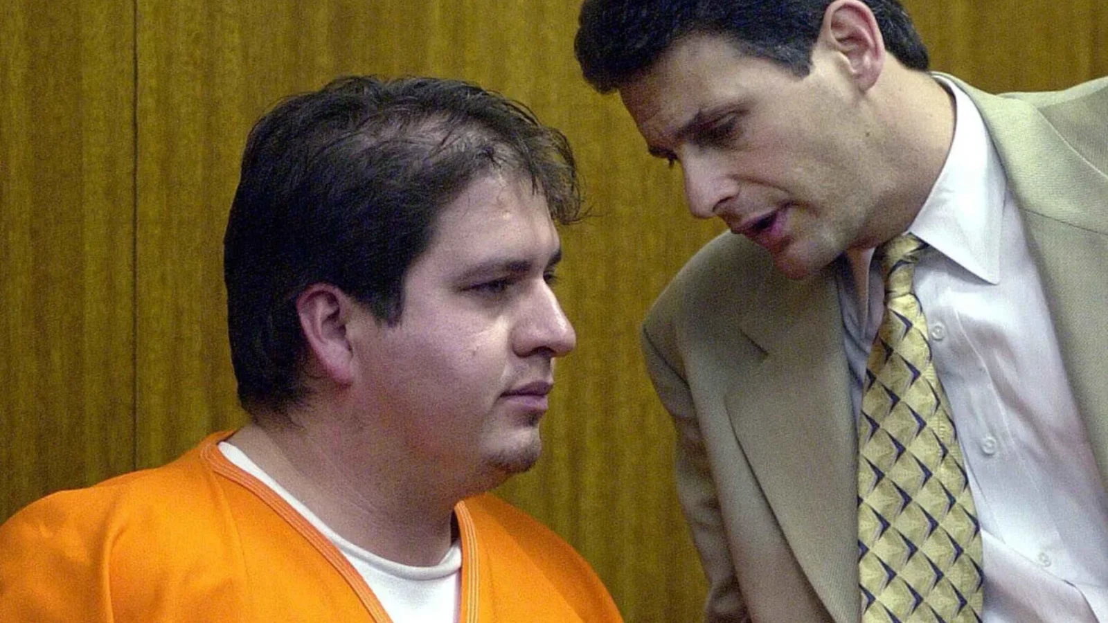 Efren Saldivar in an orange jail jumpsuit in court as a man in a suit leans in to speak to him