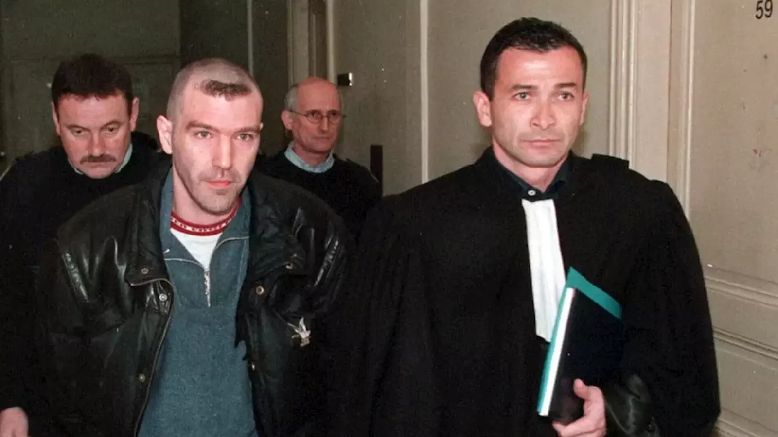 Patrice Alègre, head shaved, in a leather jacket, led through a courthouse corridor beside a lawyer in robes