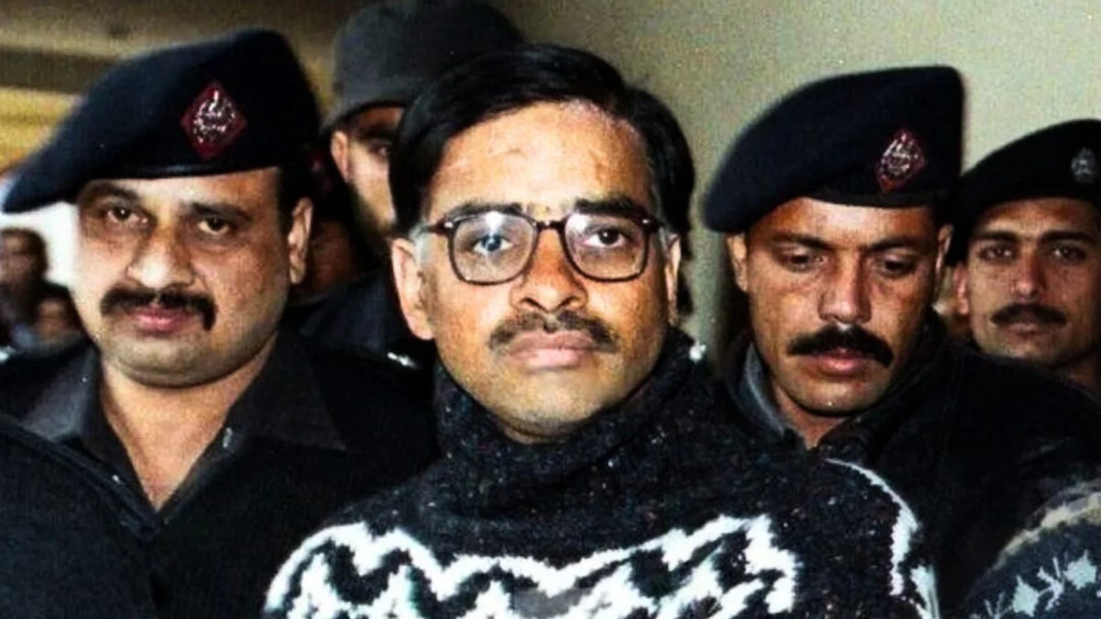 Javed Iqbal, in glasses and a patterned sweater, surrounded by police officers after his 1999 surrender