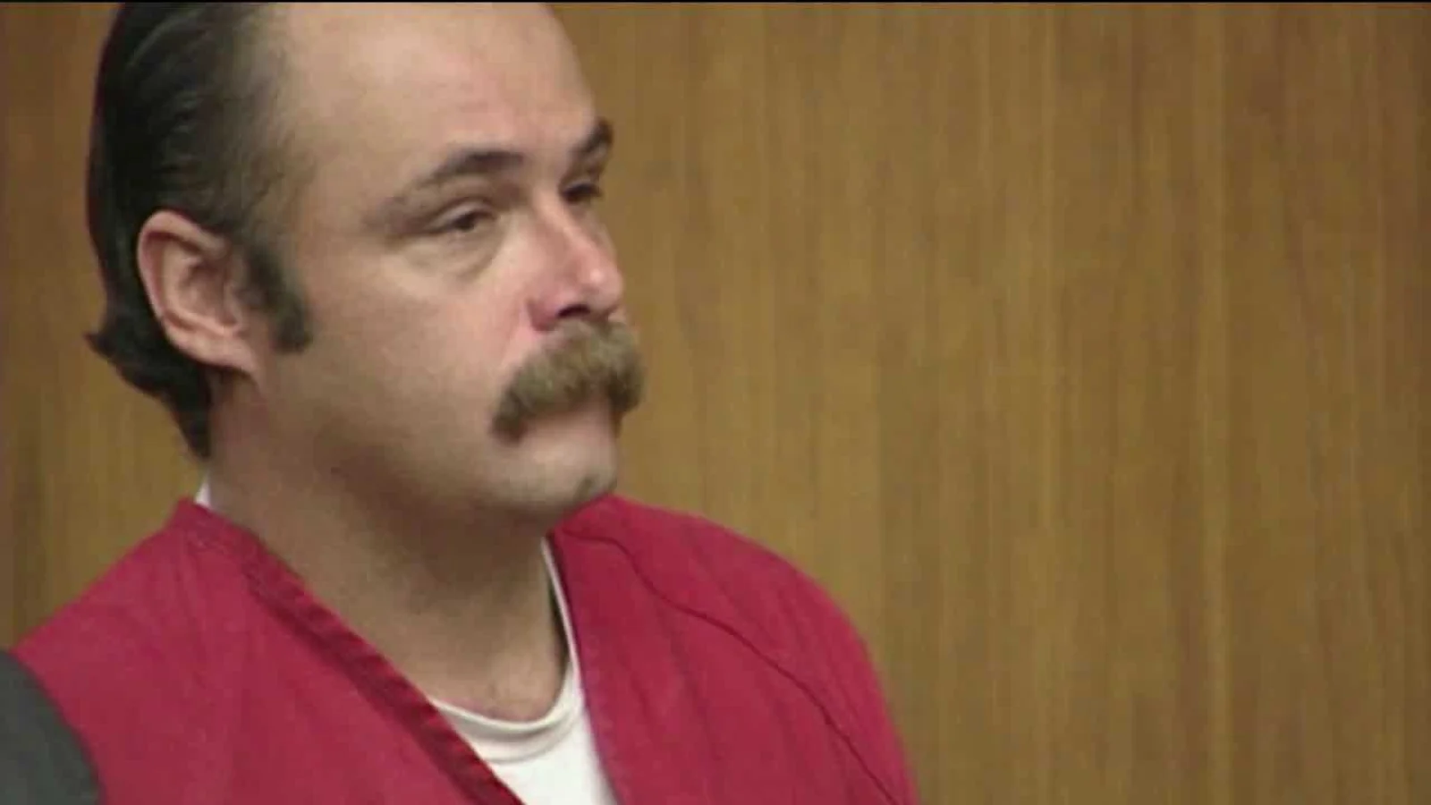 Wesley Shermantine, with a heavy mustache and slicked-back hair, in a red jail jumpsuit in a courtroom