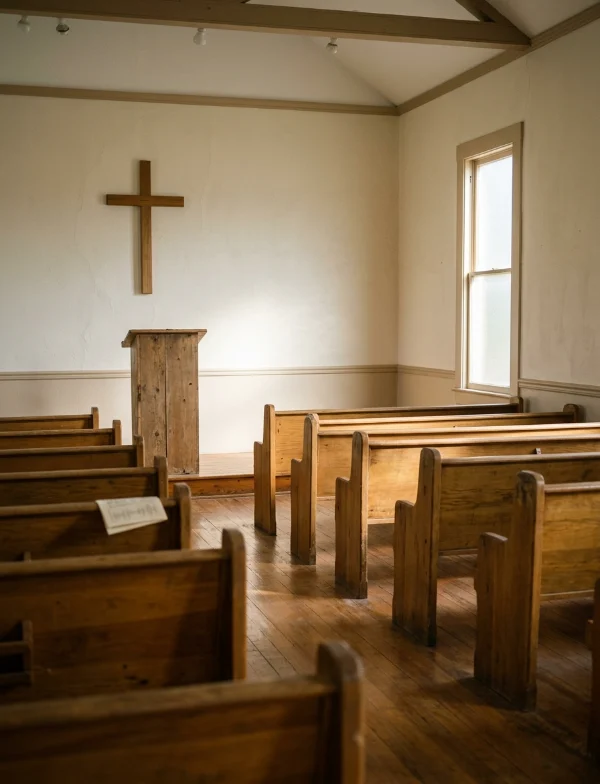 Illustration of empty wooden pews and a plain cross in a small, sunlit chapel. Not the actual prison chapel.