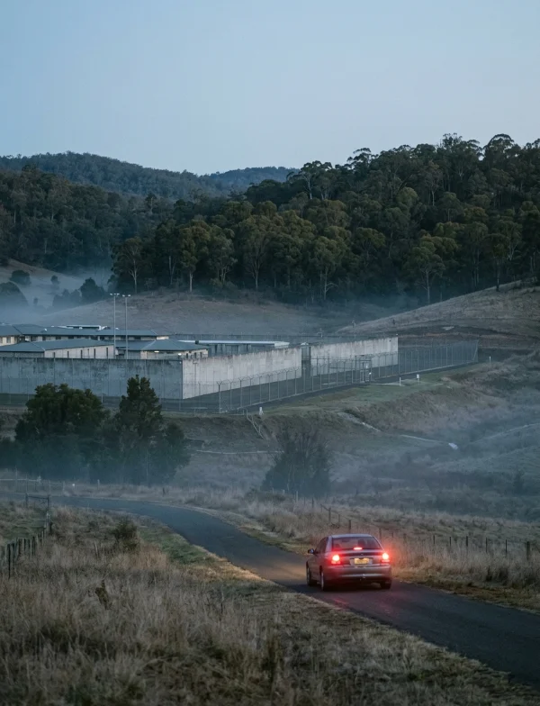 Illustration of a car on a country road leading to a walled prison in misty New South Wales hills at dusk. Not an actual scene from the case.